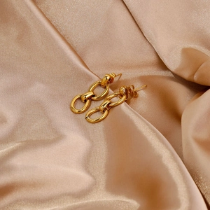 Vue détaillée de boucles d'oreilles dorées sur un tissu en satin de soie champagne