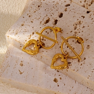 Detail of gold-plated pig nose link earrings with hammered heart charms on stone