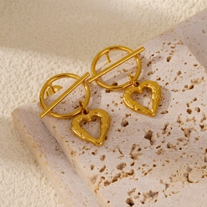 Detail of gold-plated heart earrings with lava texture on a minimalist stone surface