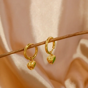 Close-up of gold heart drop earrings hanging on branches with silk background