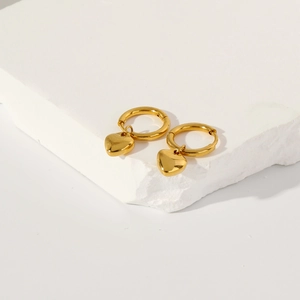 Macro shot of polished gold heart pendants on a textured white stone platform