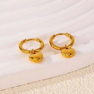 Polished gold heart drop earrings with round hoop buckles on a marble pedestal