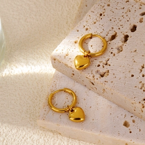 Detailed close-up of golden heart pendant earrings on beige travertine stone with natural light