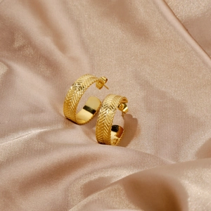 Close-up of golden C-shaped hoop earrings featuring a vintage woven herringbone texture
