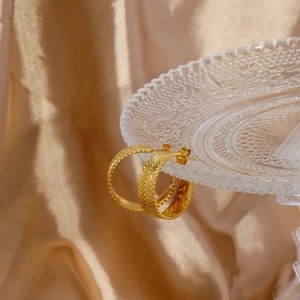 Detailed view of golden hoop earrings with intricate wheat ear pattern on satin background