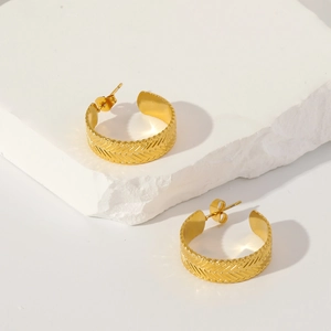 Macro shot of gold C-hoop earrings with herringbone texture on white stone base