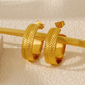 Detail of gold C-shaped hoop earrings with vintage herringbone texture on metal surface