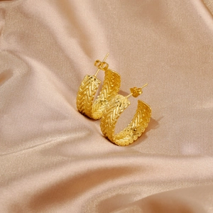 Macro view of C-shaped hoop earrings with woven texture on luxury champagne silk fabric
