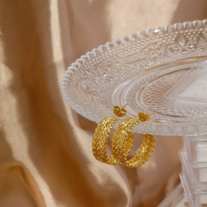 Detailed view of gold C-shaped twisted earrings with woven texture on a glass tray