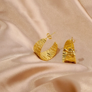Detailed view of gold C-shaped earrings with fluid ripple texture on champagne satin