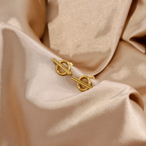 Detailed view of gold OT buckle earrings resting on champagne silk fabric background