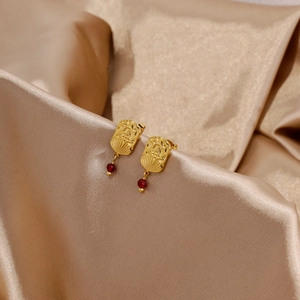 Detail of 18k gold earrings with hammered texture and red gemstone on silk