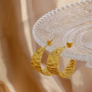 Detail of golden C-shaped leaf earrings with textured finish on a glass tray