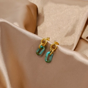 Détail de boucles d'oreilles en acrylique vert et or sur un élégant tissu de satin champagne
