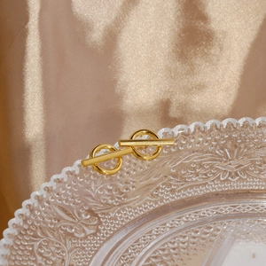 Close-up of golden toggle earrings on glass tray with elegant silk background