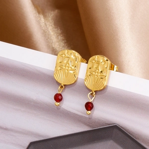 Detail of 18k gold earrings with embossed star pendant and hanging red gemstone bead