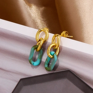 Gros plan de boucles d'oreilles géométriques en acrylique avec anneaux dorés et pendants verts