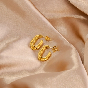Detalle de pendientes de doble aro ovalado dorado sobre elegante fondo de tela de seda