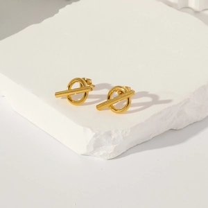 Close-up of golden geometric OT circle earrings on a minimalist stone display stand