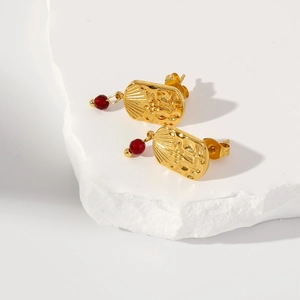 Macro view of 18k gold earrings with sunburst texture and red enamel drop charm