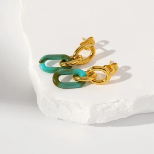 Détail de boucles d'oreilles en acrylique émeraude et or sur fond de pierre blanche