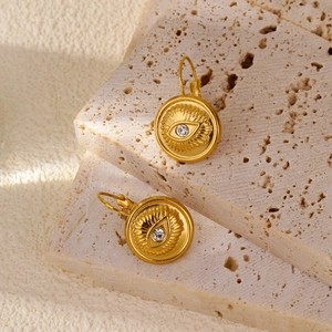 Gros plan de boucles d'oreilles Œil du Mal en or 18k avec zircons sur pierre travertin