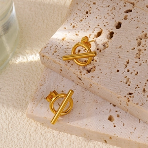 Close-up of golden geometric T-bar and ring earrings on natural travertine stone