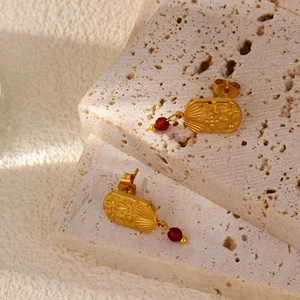 Detail of 18k gold earrings with vintage embossed floral pattern and deep red gemstone drop