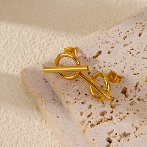 Close-up of gold geometric OT buckle earrings on a natural stone background