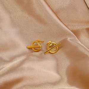 Detailed macro view of polished gold geometric OT hoop earrings on soft champagne silk