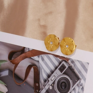 Détail de boucles d'oreilles tournesol dorées mates avec zircon sur tissu en soie