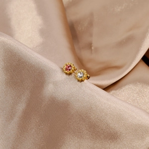 Detail of 18k gold sunflower earrings with ruby and white zircon on champagne silk