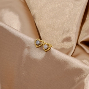 Vue macro de boucles d'oreilles cœur en or et pierre blanche sur satin champagne