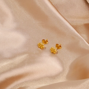 Dettaglio di orecchini a lobo a forma di girasole dorato su lussuosa seta color champagne