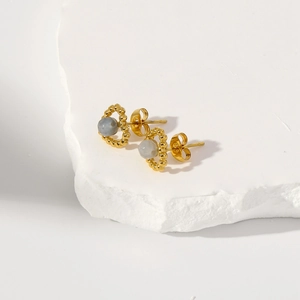 Détails de boucles d'oreilles dorées avec pierres grises sur fond de pierre texturée