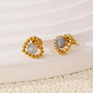 Gros plan de boucles d'oreilles cœur dorées avec pierre grise et texture perlée rétro