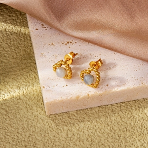 Détail de boucles d'oreilles cœur dorées avec pierre blanche sur surface en soie texturée