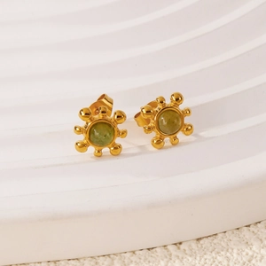 Détail macro d'une boucle d'oreille dorée avec pierre verte sur socle blanc