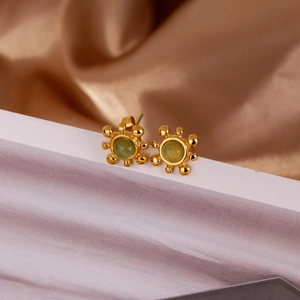 Détail macro de boucles d'oreilles soleil dorées avec une pierre précieuse verte