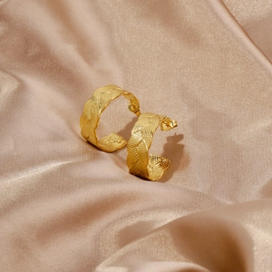 Close-up of 18K gold leaf textured C-shape earrings on elegant champagne silk fabric