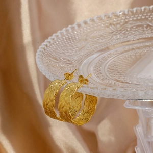 Detailed view of 18K gold phoenix leaf textured hoop earrings with woven design