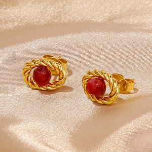 Detailed macro view of 18k gold braided earrings with oval red ruby inlay on silk fabric