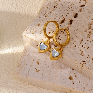 Detailed view of 18k gold heart earrings with crystal stones on travertine stone background