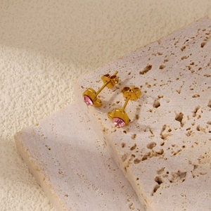 Vue macro détaillée de clous d'oreilles cœur dorés avec cristaux roses sur pierre