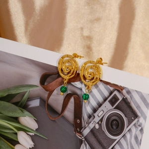 Detailed shot of 18k gold spiral earrings with green malachite bead on vintage magazine