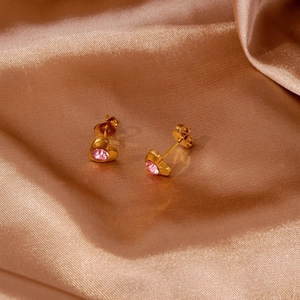 Gros plan de boucles d'oreilles cœur dorées 18 carats avec zircon rose sur satin