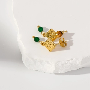 Dettaglio di orecchini dorati con texture lavica e perle verde smeraldo