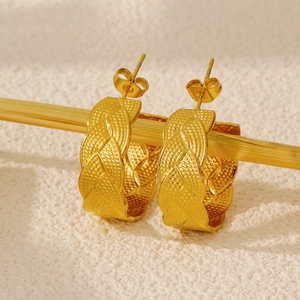 Macro detail of golden C-shaped woven earrings with vintage leaf pattern and textured finish