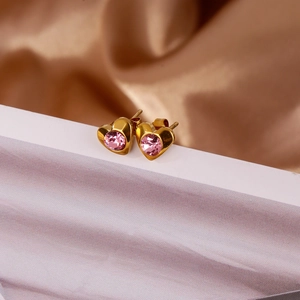 Détail de boucles d'oreilles cœur en or avec cristal rose sur un tissu de soie