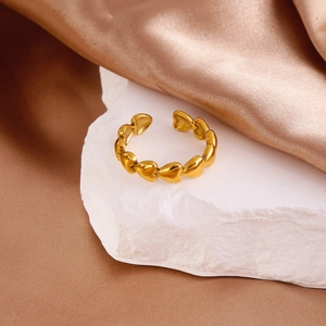 Detail shot of a gold heart-shaped ring displayed on stone with brown silk background